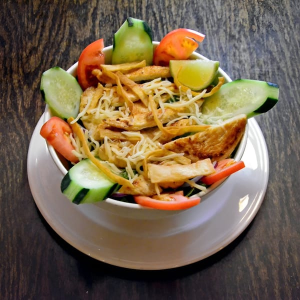 Mexican chicken salad with tortilla strips, cheese, tomatoes, cucumbers, and lime.