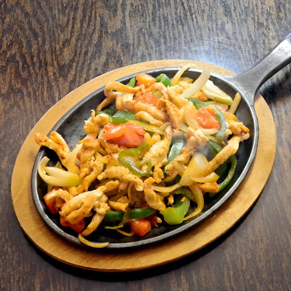 Sizzling chicken fajitas with green peppers, onions, and tomatoes in a cast iron skillet.
