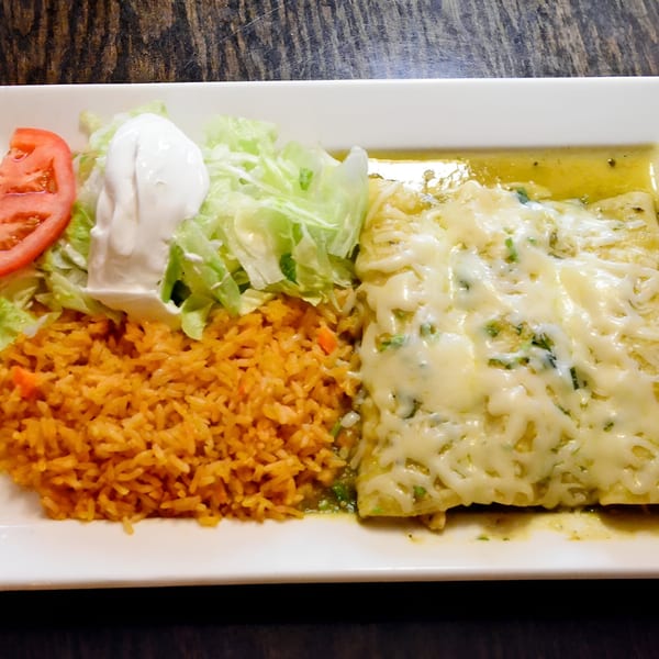 Mexican enchiladas with green sauce and melted cheese, served with rice, lettuce, tomato, and sour cream.