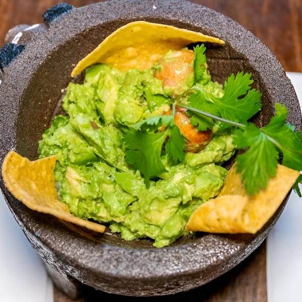 Fresh guacamole with cilantro and tortilla chips in a traditional molcajete bowl.