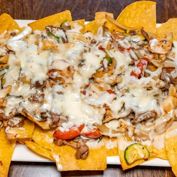 Los Amigos Don Juan's nachos with melted white cheese, meat, and vegetables on a white plate.